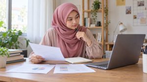 Ilustrasi calon mahasiswa berhijab meninjau catatan dan laptop untuk pembahasan jurusan favorit di UIN Raden Fatah Palembang.